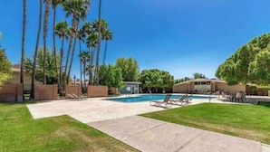 Ein wohnlicher Garten mit Pool, Palmen und Rasen.