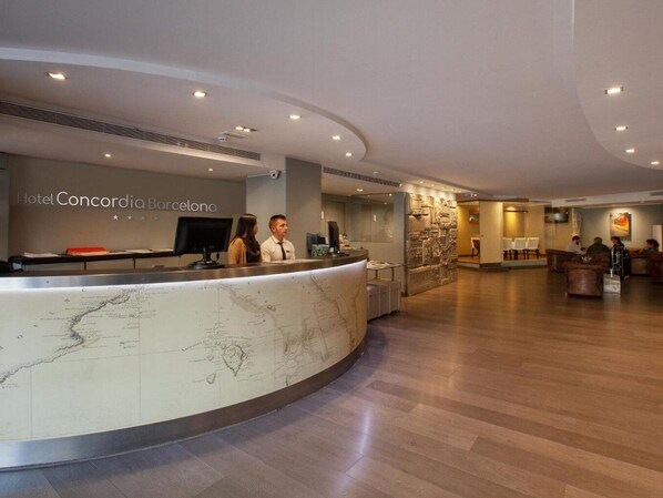 Un'area reception di un hotel con un bancone in marmo, una grande mappa del mondo e un salotto con divani.