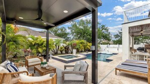 A covered outdoor patio with wicker furniture, a pool, and lush greenery.