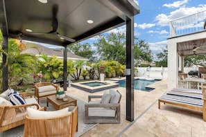 A covered outdoor patio with wicker furniture, a pool, and lush greenery. - Luxury Home W/ Pool Spa & Pool Heated Near IMG & Beach (Bradenton)