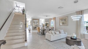 A spacious living area with a staircase, a dining area, and a modern light fixture.