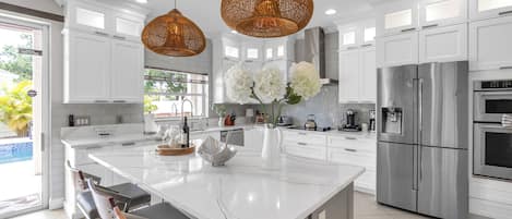 A modern kitchen with white cabinetry, a large island, stainless steel appliances, and wicker pendant lighting.