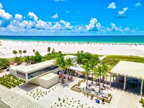 A beachside hotel with a modern design, featuring a spacious patio area with palm trees, a pool, and a view of the beach and ocean. - Luxury Home W/ Pool Spa & Pool Heated Near IMG & Beach (Bradenton)