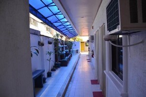 Un pasillo estrecho con techo azulado, plantas en macetas y un banco.