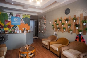 A reception area with a wooden reception desk, wicker chairs, a clock, and potted plants on the wall.