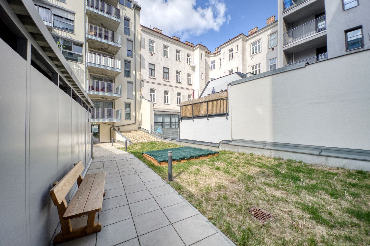 Une cour avec un banc, un petit espace gazonné et une piscine.