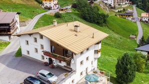 Ein mehrstöckiges Gebäude mit einem Balkon, einer überdachten Außenbereich-Sitzgelegenheit und einem Parkplatz mit Autos.