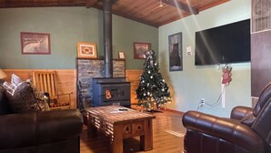 A cozy living room with a fireplace, a Christmas tree, and a large flat-screen TV. - Roadrunner - Historic Upper Canyon, Priv Hot Tub, Cozy (Ruidoso)