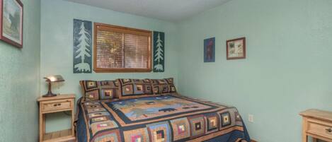 Un dormitorio con cama, una mesita de noche, una lámpara, una ventana con persianas e imágenes enmarcadas en la pared.