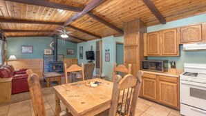 A cozy room with a wooden ceiling, a dining table with chairs, a red sofa, a fireplace, and a kitchen area with wooden cabinets and appliances. - Roadrunner - Historic Upper Canyon, Priv Hot Tub, Cozy (Ruidoso)