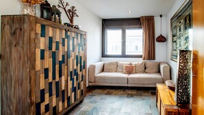 Ein gemütliches Wohnzimmer mit einem Holzkabinett, einem beigefarbenen Sofa und einem gemusterten Teppich.