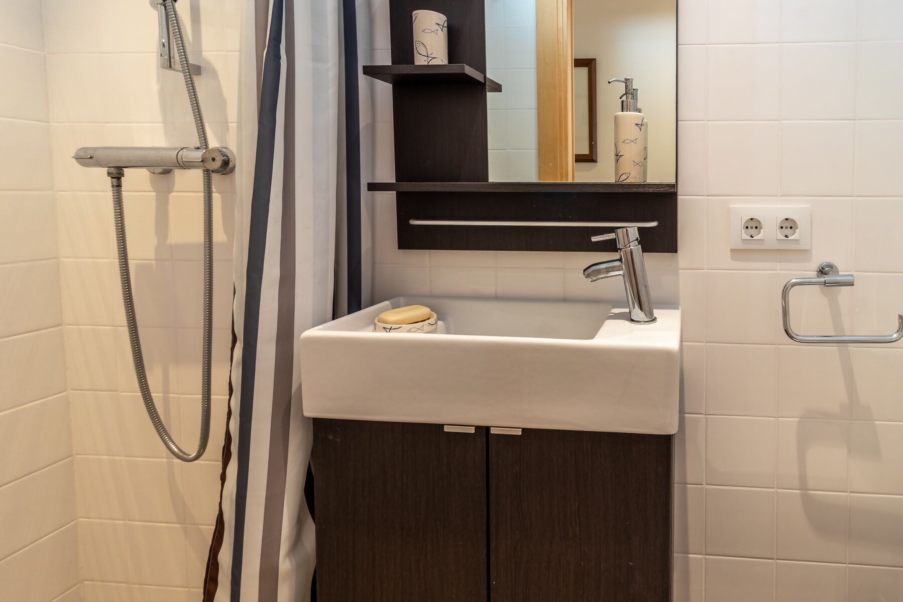 Un baño con ducha, lavabo, espejo y toallero.