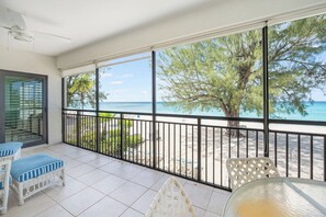 Balkon med udsigt over stranden, hvide fliset gulve og udendørs møbler.