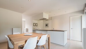 Una cocina moderna con armarios blancos, una mesa de comedor de madera y sillas blancas.