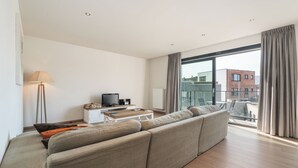 Una sala moderna con un sofá grande, un televisor y un balcón con cortinas.