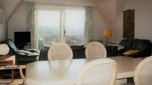 A living room with a dining table, chairs, a sofa, a television, and a window with curtains. - Golf & Beach C2 - beautiful 3-bedroom apartment 50 m from the beach (De Haan)