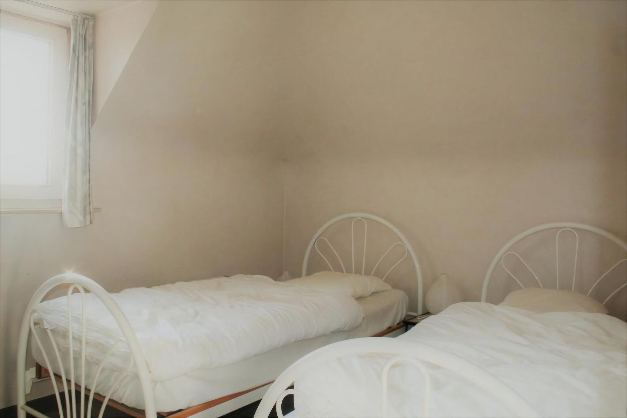 Two single beds with metal frames in a room with plain walls and a window.