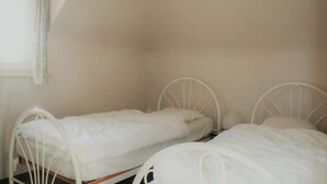 Two single beds with metal frames in a room with plain walls and a window. - Golf & Beach C2 - beautiful 3-bedroom apartment 50 m from the beach (De Haan)