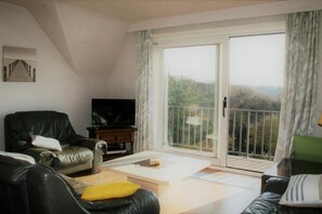 Ein Wohnzimmer mit Fernseher, einer Couch, einem Couchtisch und einer Schiebetür zum Balkon.