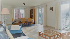 Ein Wohnzimmer mit einer Couch, einem Couchtisch, einem Esstisch mit Stühlen, einer Lampe und einem Bücherregal.