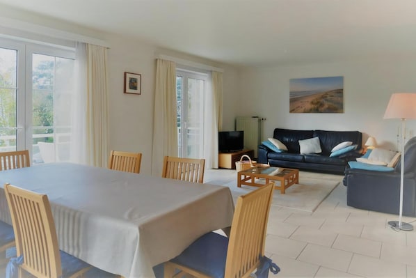 A room with a dining table, chairs, a sofa, a TV, and a lamp.