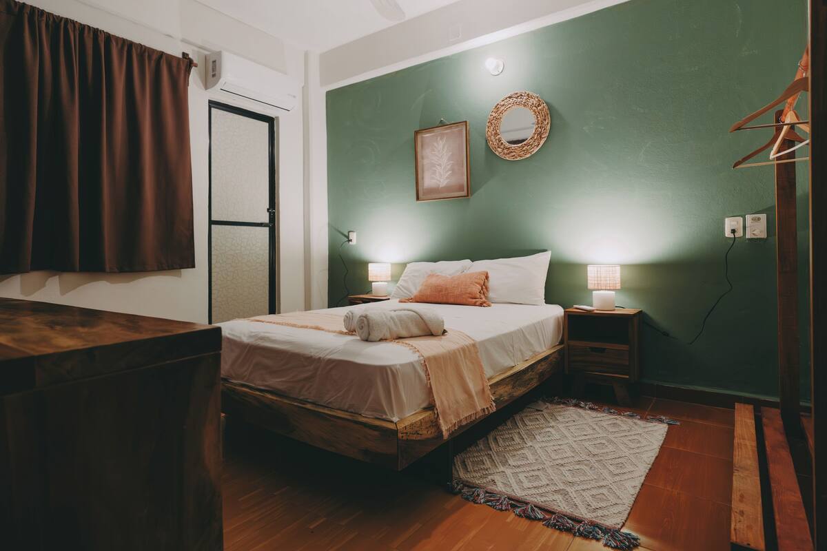 A bedroom with a bed, bedside tables, a wall-mounted mirror, and a door.