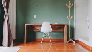 Una habitación con un escritorio de madera, una silla blanca, un perchero de madera y una pared verde.