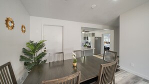 Comedor con una mesa y sillas de madera oscura, una planta en maceta y una puerta blanca.