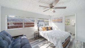Un dormitorio con una cama, ventilador de techo, ventana con persianas y una puerta.