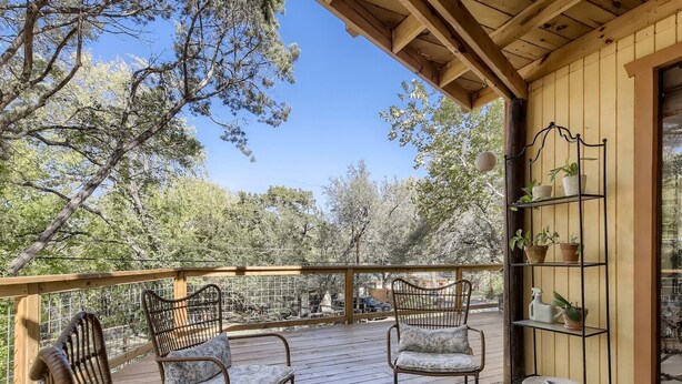 A wooden deck with wicker chairs and a round table, surrounded by potted plants and a view of trees. - The Yellow Treehouse by the Lake - NO CLEANING FEES!!! (Austin)