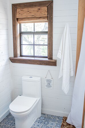 A bathroom with a white toilet, a window with a wooden frame, and a hanging towel. - The Yellow Treehouse by the Lake - NO CLEANING FEES!!! (Austin)