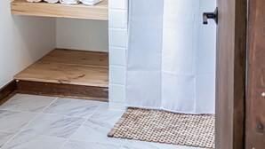 A bathroom with wooden shelves holding rolled towels and white baskets, a shower curtain, and a small wooden mat. - The Yellow Treehouse by the Lake - NO CLEANING FEES!!! (Austin)