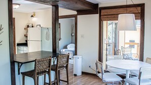 A dining area with a dark wooden table and wicker chairs, a white round table with metal chairs, and a large hanging light fixture. - The Yellow Treehouse by the Lake - NO CLEANING FEES!!! (Austin)