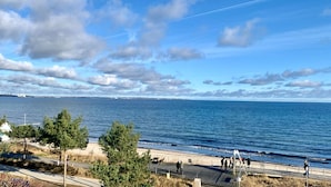 Vista costera con cielo despejado, una playa y un paseo marítimo con gente caminando.