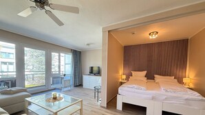 Una habitación de hotel moderna con una cama, una mesa de centro de vidrio, un sofá, un televisor y un balcón con vistas.