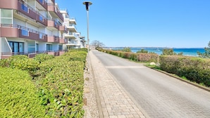 Un hotel de varios pisos con balcones, un camino empedrado y vista al mar.