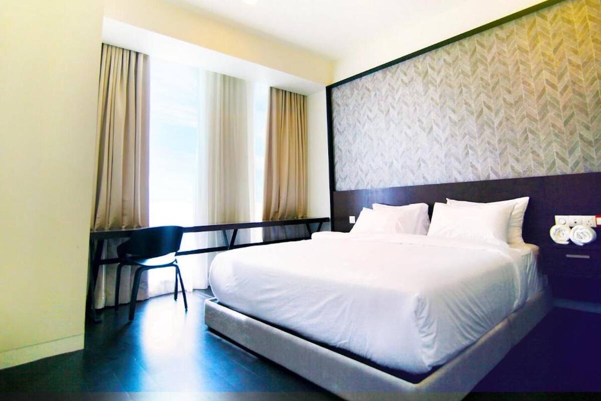 Ein Hotelzimmer mit einem großen Bett, einem Sessel und einem Fenster mit Vorhängen.