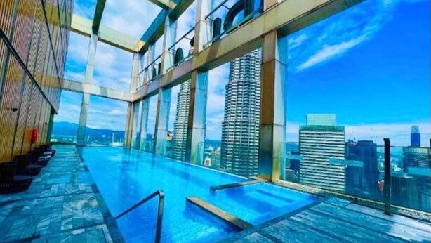 Une piscine à débordement située sur le toit, offrant une vue sur la ville, une architecture moderne et un ciel dégagé.