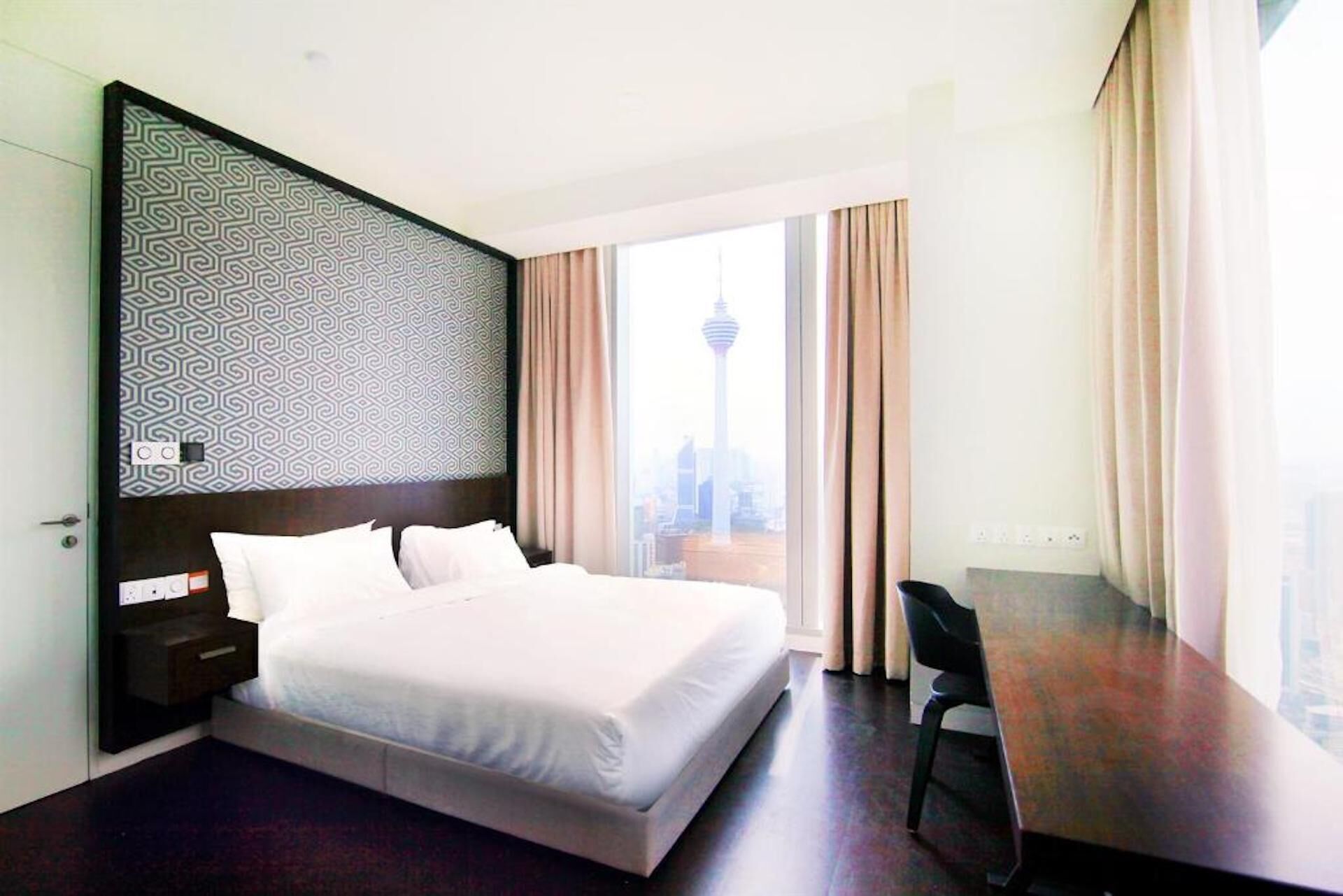 A hotel room with a large bed, a desk, and a view of a cityscape.