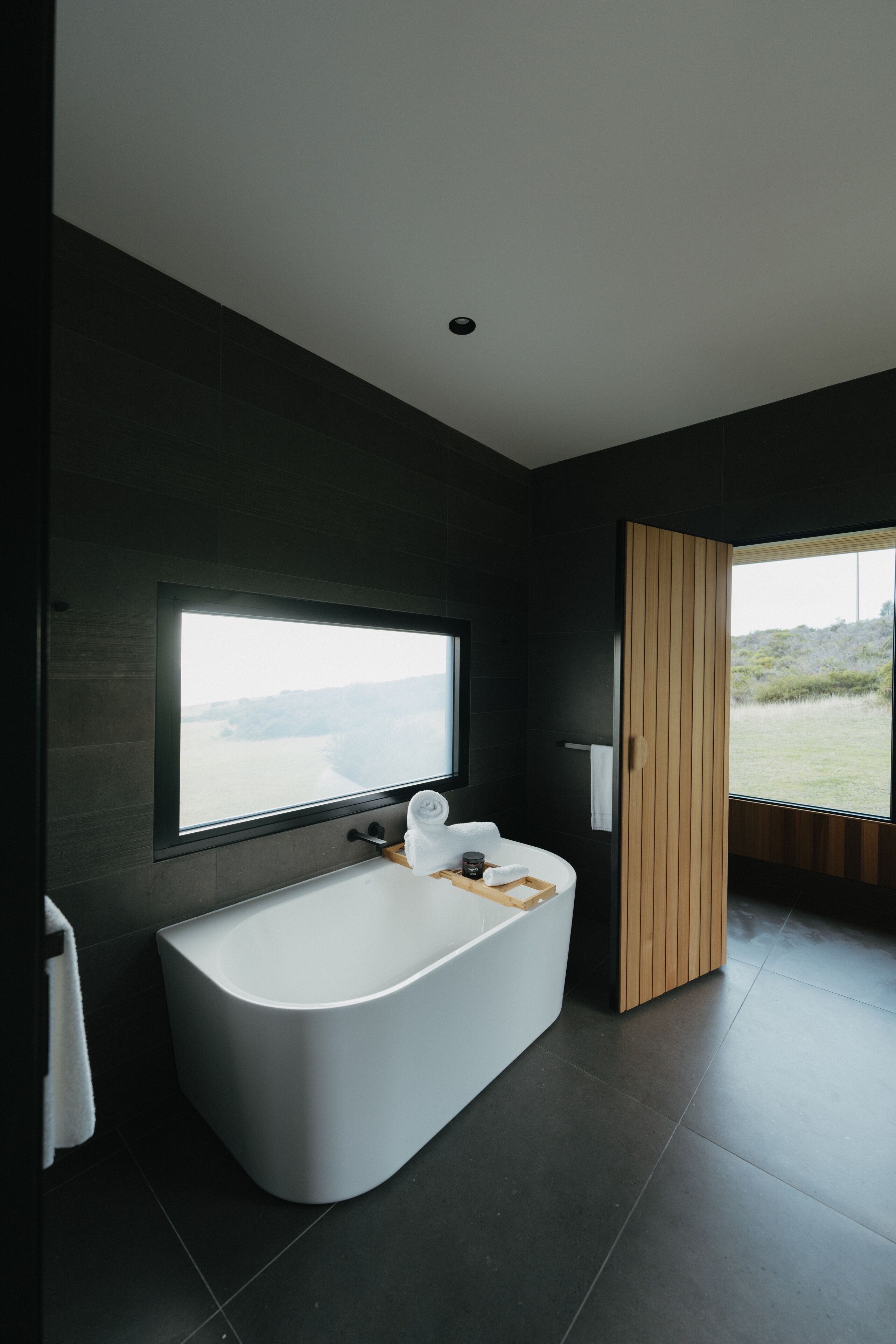 A modern bathroom with a freestanding bathtub, a large window, and a view of the outdoors.