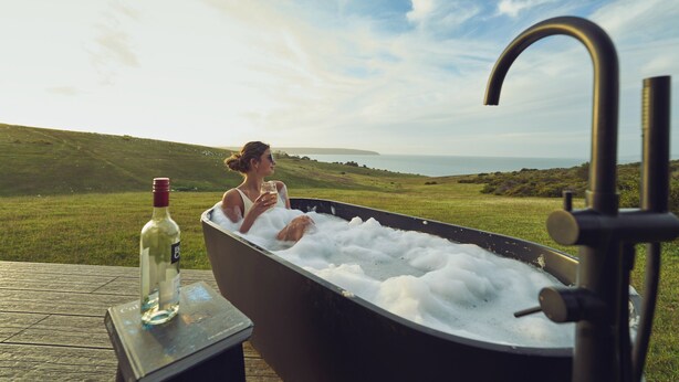 A person relaxing in a hot tub with a bottle of wine on a table beside it, overlooking a scenic landscape. - CABN Kangaroo Island Ocean View Private Off Grid Luxury Accommodation (Willoughby)