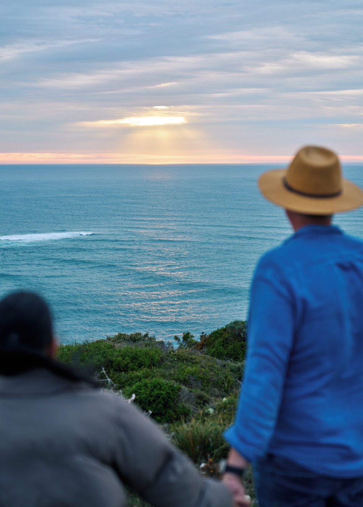 Two people overlooking a coastal view with the ocean and a sunset.