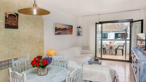 Ein gemütliches Wohnzimmer mit Essbereich, einer Couch, einem kleinen Tisch mit Blumen und Blick durch eine Glastür auf eine Terrasse.