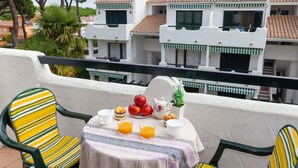 Ein Balkon mit Tisch, gedeckt für das Frühstück, mit einem gestreiften Stuhl, einer Tischdecke und verschiedenen Frühstücksangeboten.