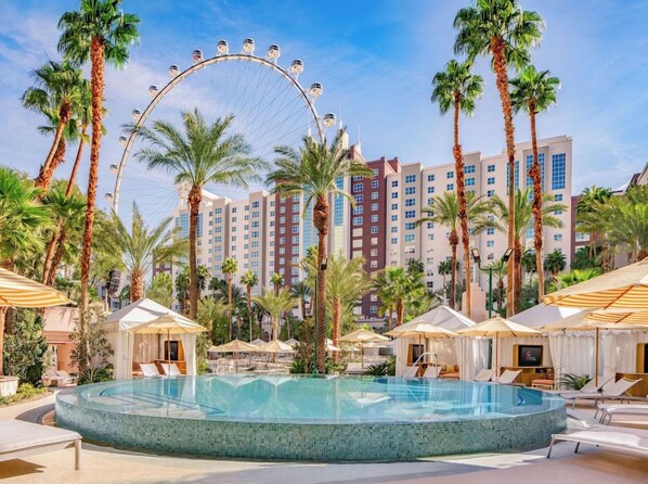 A hotel pool area with a Ferris wheel, palm trees, and a large building in the background. - Two Queen Room at a Hotel (Las Vegas)