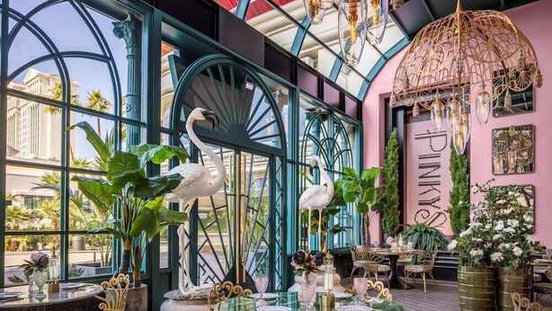 Un restaurante con amplios ventanales de vidrio, barandillas de metal ornamentadas y una pared rosa con el nombre 'Pinkys'.
