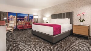 Hotellihuone, jossa on suuri sänky, työpöytä, tuoli ja näkymä kaupunkimaisemaan.