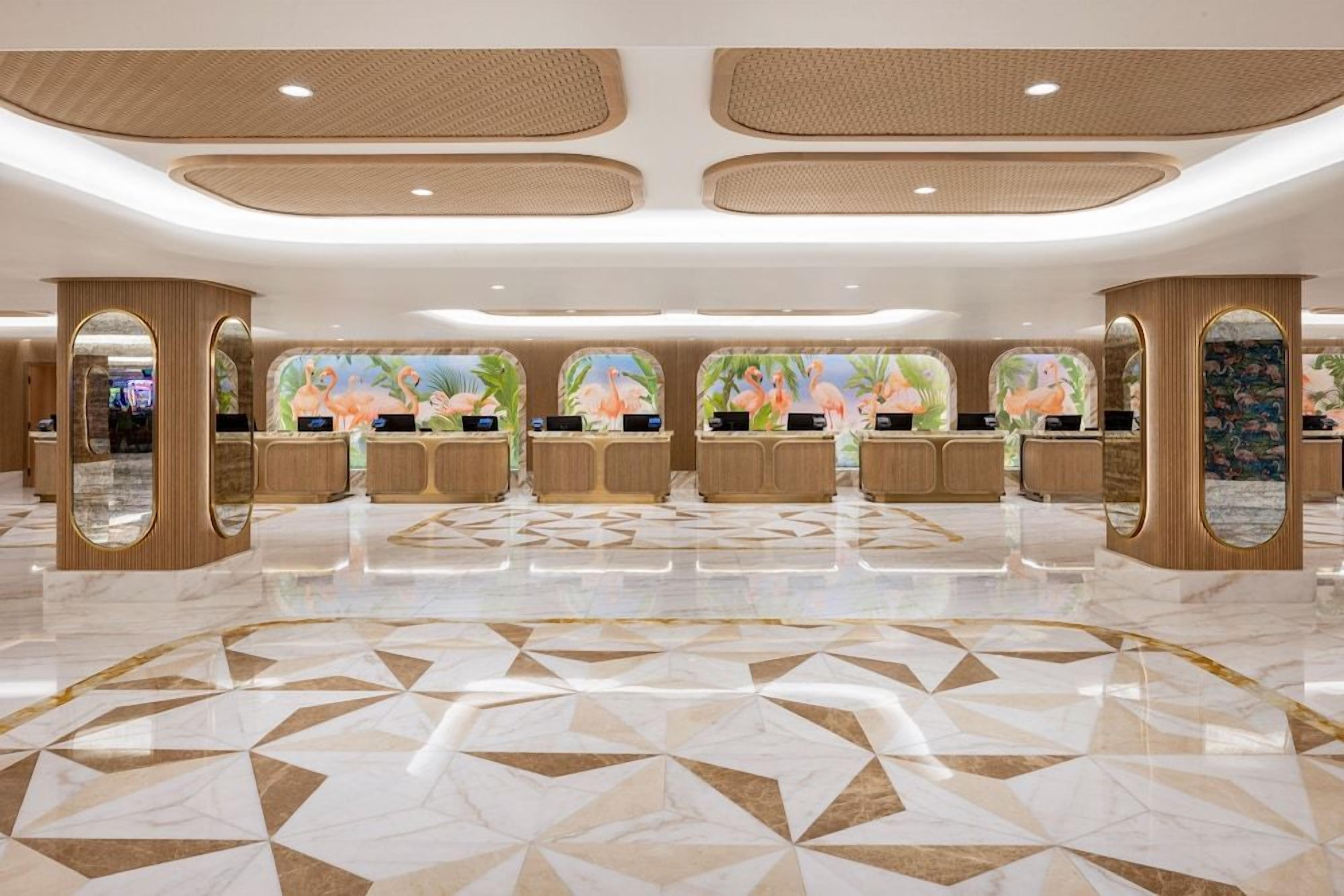 A hotel lobby with a geometric patterned floor, wooden reception desks, and decorative wall murals.