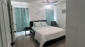 Un dormitorio con cama, ventilador de techo, mesita de noche y una puerta.