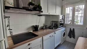 A compact kitchen with white cabinets, a black countertop, a washing machine, and a window with a view of the outside. - Casa Alfonso Toledo - Más que una casa, un hogar (Toledo)